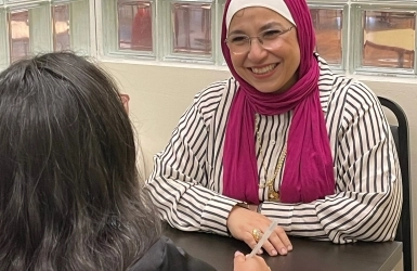 A front view of a woman sitting at a chair smiling while in a conversation